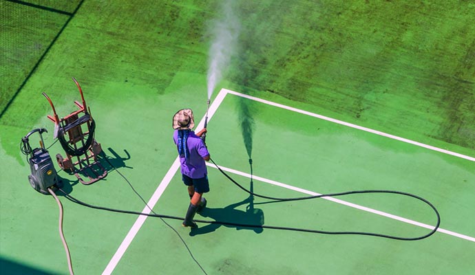 male worker washing a tennis court from a hose