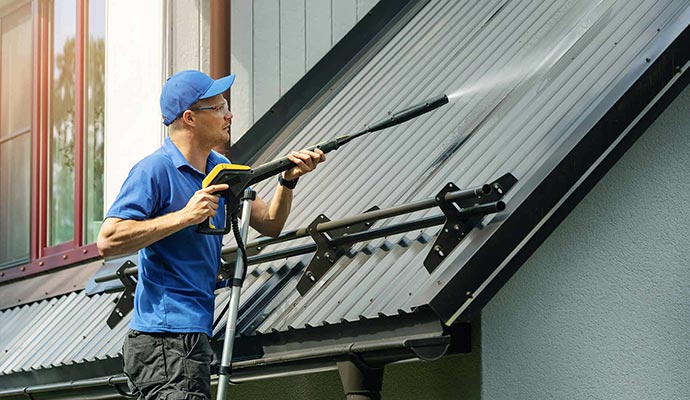 man standing on ladder and cleaning house metal roof with power washer