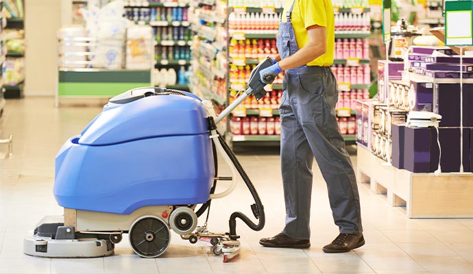 worker cleaning retail store floor with machine